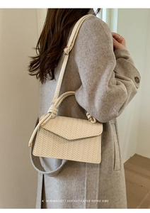 Detail of off-white woven shoulder bag with adjustable strap and knotted top handle
