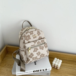 Detail eines Mini-Rucksacks mit Blumenmuster, Gold-Reißverschlüssen auf Buch und Holzregal