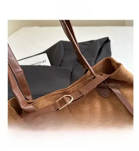 Detail view of brown faux suede tote bag with contrast leather strap and gold buckle