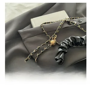 Detail of black pleated bag featuring golden chain strap and adjustable spherical metal ball