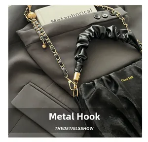 Detail of the golden hardware hook and leather chain on a black pleated velvet bag