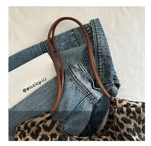 Detalle del bolso tote con estampado de leopardo y asas de cuero marrón sobre tela