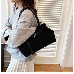 Close-up of large black matte tote bag with gold hardware worn by a model in soft lighting