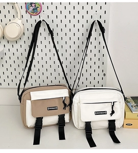 Detail of khaki and white canvas messenger bags with dual buckle closure and front zip pocket