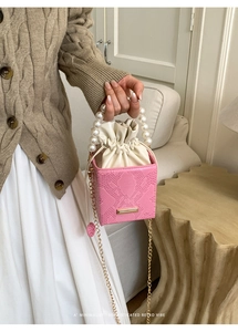 Dettaglio borsa a secchiello rosa effetto serpente con manico di perle e catena d'oro