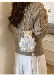 Detail of cream snake-embossed crossbody bag with large pearl handle and gold chain