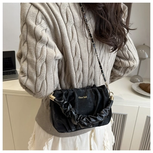 Detail of a black pleated cloud bag with gold chain strap on a model wearing knitwear