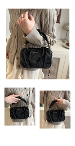 Detail view of black pleated handbag with gold hardware and chain strap on beige cardigan