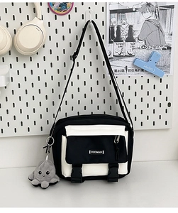 Detail of black and white messenger bag with dual buckles and a plush octopus pendant