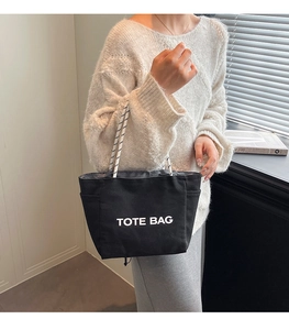 Detailed view of black canvas tote bag with white text print and rope shoulder straps