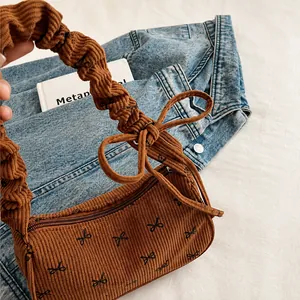 Detail of brown corduroy bag with black bow prints and ruffled handle on denim fabric