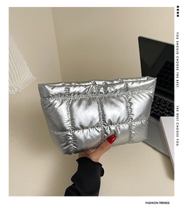 Close-up of a silver quilted clutch bag with metallic finish held by a model in a trendy setting
