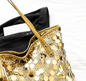 Detail of gold sequin tote bag with leather strap and rivet accents on white fabric