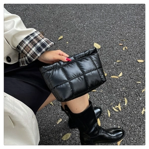 Close-up of black quilted puffer clutch bag with shiny nylon finish in outdoor setting