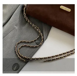 Detail of dark brown suede tote bag with golden metal chain strap on gray blazer