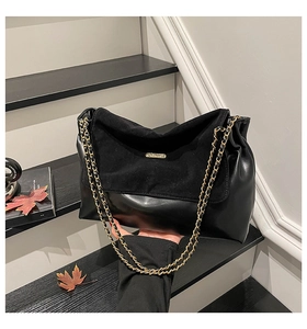 Detail of black suede patchwork tote bag with gold chain strap in autumn setting