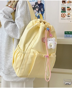 Close-up of light yellow nylon backpack featuring drawstring closure and plush bear pendant