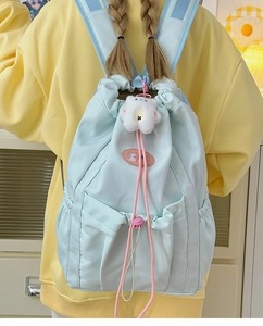 Detail of light blue nylon backpack with drawstring closure and cute plush bear accessory