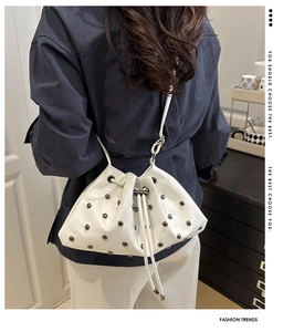 Rear view of a white drawstring bucket bag with black rivets on matte faux leather