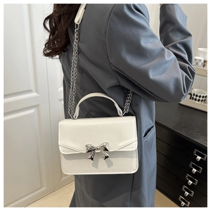 Detail view of a white minimalist crossbody bag with a silver metallic bow decoration