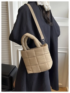 Quilted tan down tote bag shown over shoulder of model in a stylish black coat