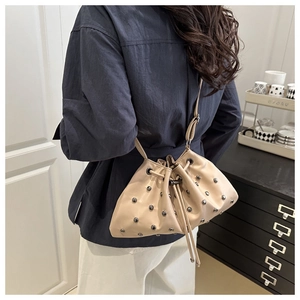 Detailed close-up of beige drawstring bucket bag with decorative silver-tone metal rivets