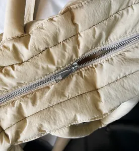 Close-up of smooth metal zipper detail on beige quilted padded puffer handbag