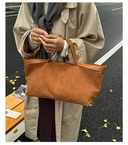 Detail of caramel suede tote bag with leather trim held by model in autumn street setting