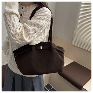 Detail of a dark brown suede tote bag featuring a bow and gold metal buckle