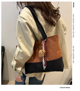 Detalle de un bolso tote grande bicolor en ante marrón y lona negra con colgante de osito