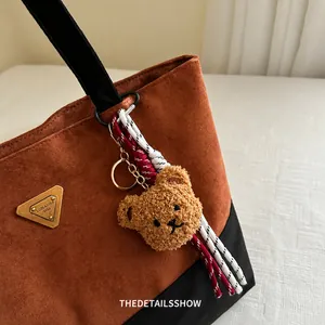 Detalle de un colgante de oso peludo con cuerda tricolor en un bolso de ante suave