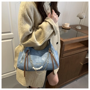 Detalle de bolso de hombro denim con perlas y cadena dorada sobre un abrigo beige