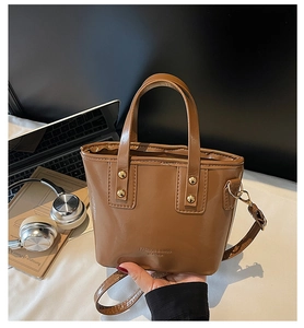 Bruine lederen bucket bag naast een laptop en koptelefoon voor dagelijks gebruik