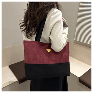 Detalle de bolso tote de ante burdeos y negro con logo de triángulo dorado en modelo
