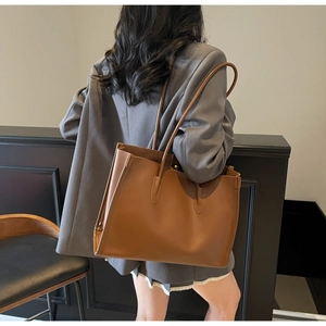 Detail of a large brown tote bag with slim shoulder straps worn by a model in a café setting