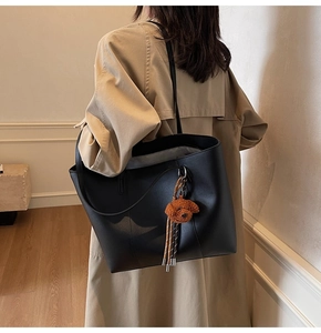Detalle de un bolso tote negro grande con un tierno colgante de oso de peluche marrón y acabado liso