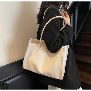 Detail of minimalist cream tote bag showing reinforced side stitching and slim shoulder straps