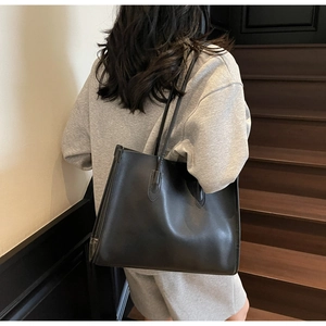 Minimalist large black tote bag showcased on a shoulder in a stylish lifestyle setting