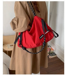 Vue détaillée du sac fourre-tout en nylon rouge avec bandoulière noire et étiquette