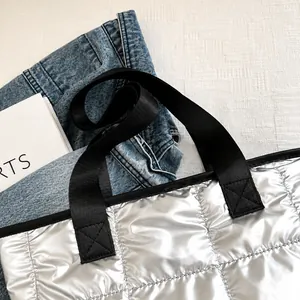 Detail van zilveren gewatteerde draagtas met metallic textuur en zwarte handvatten