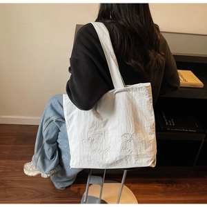 Detail of a large white canvas tote bag with heart and star prints worn over the shoulder