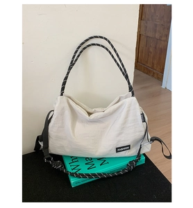 Détail du sac cabas en nylon blanc avec anses en corde rayée sur fond de livre vert