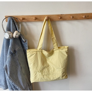 Detail of bright yellow canvas tote bag featuring delicate embroidery and long shoulder strap