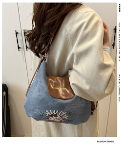 Dettaglio borsa a tracolla blu denim con patta in pelle marrone e stampa baseball