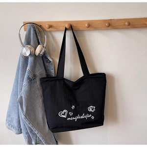 Detail of black canvas tote bag with white script lettering hanging on a wooden rack
