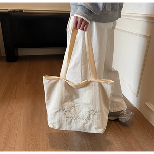 Detailed embroidery of hearts and stars on minimalist beige canvas tote bag surface