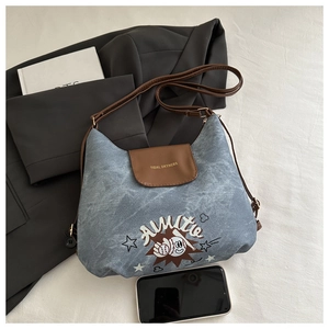 Dettaglio borsa a tracolla in denim blu con patta in pelle marrone e stampa artistica