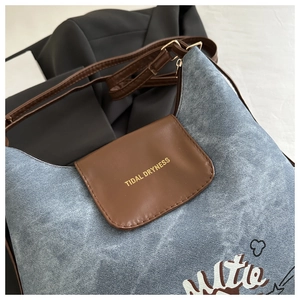 Dettaglio borsa in denim blu con patta in pelle marrone e scritta dorata