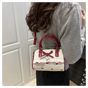 Detail of white bow-print bag with red ruffle trim and heart-shaped metal pendant