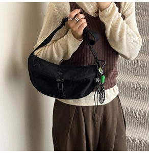 Detail of black crescent crossbody bag featuring dual zippers and checkered rope charm